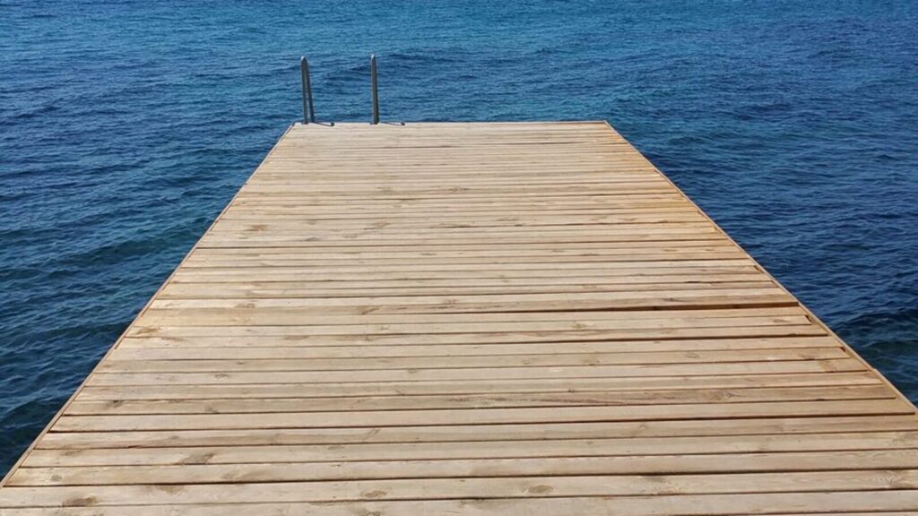 A wooden boardwalk crossing grass toward open water, one plank at a time
